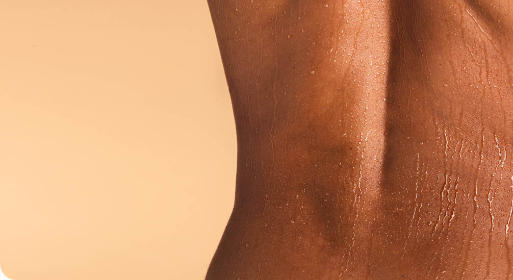 Close-up van de zijkant van een gebruinde, natte rug bedekt met waterdruppels, tegen een beige achtergrond.