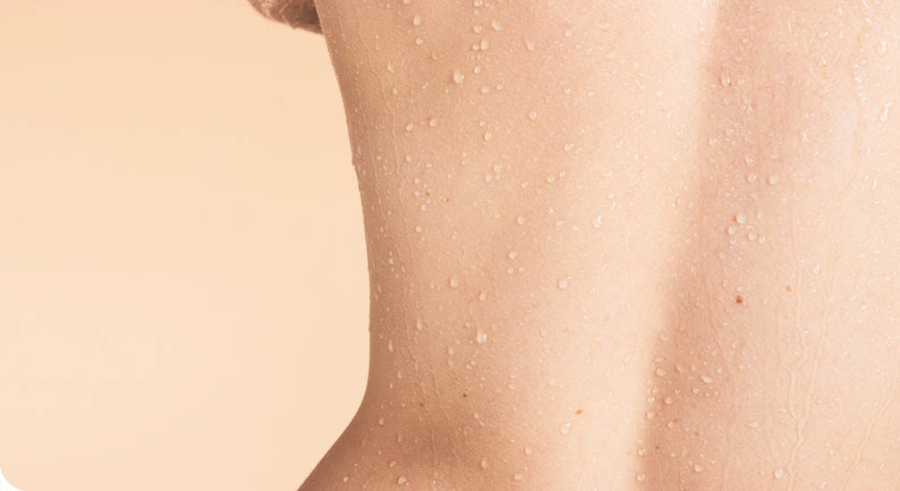 Close-up van de onderrug van een persoon met een lichte huidskleur. De huid is bedekt met kleine waterdruppeltjes.