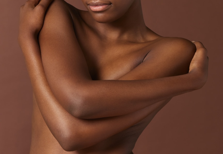 Close-up van de romp en armen van een persoon met een donkere huidskleur die zichzelf omhelst.