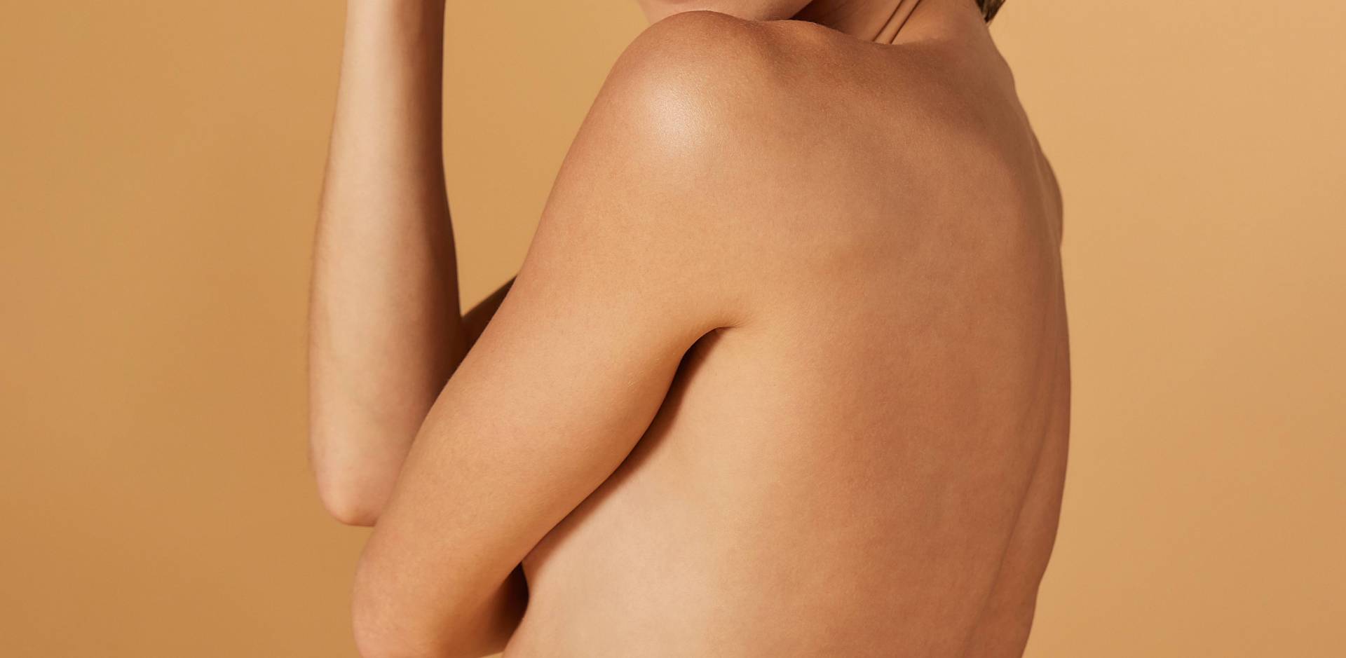 De rug en arm van een persoon met een lichte huidskleur, gezien vanaf de achterkant tegen een effen beige achtergrond.