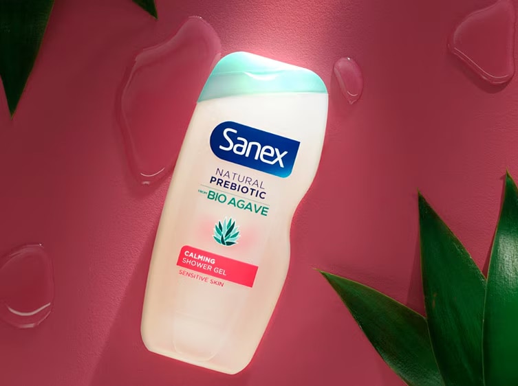Sanex Natural Prebiotic Bio Agave Calmante Douchegel met roze label op een roze achtergrond met groene bladeren. Sanex Natural Prebiotic Bio Agave Calmante Douchegel met roze label op een roze achtergrond met groene bladeren.